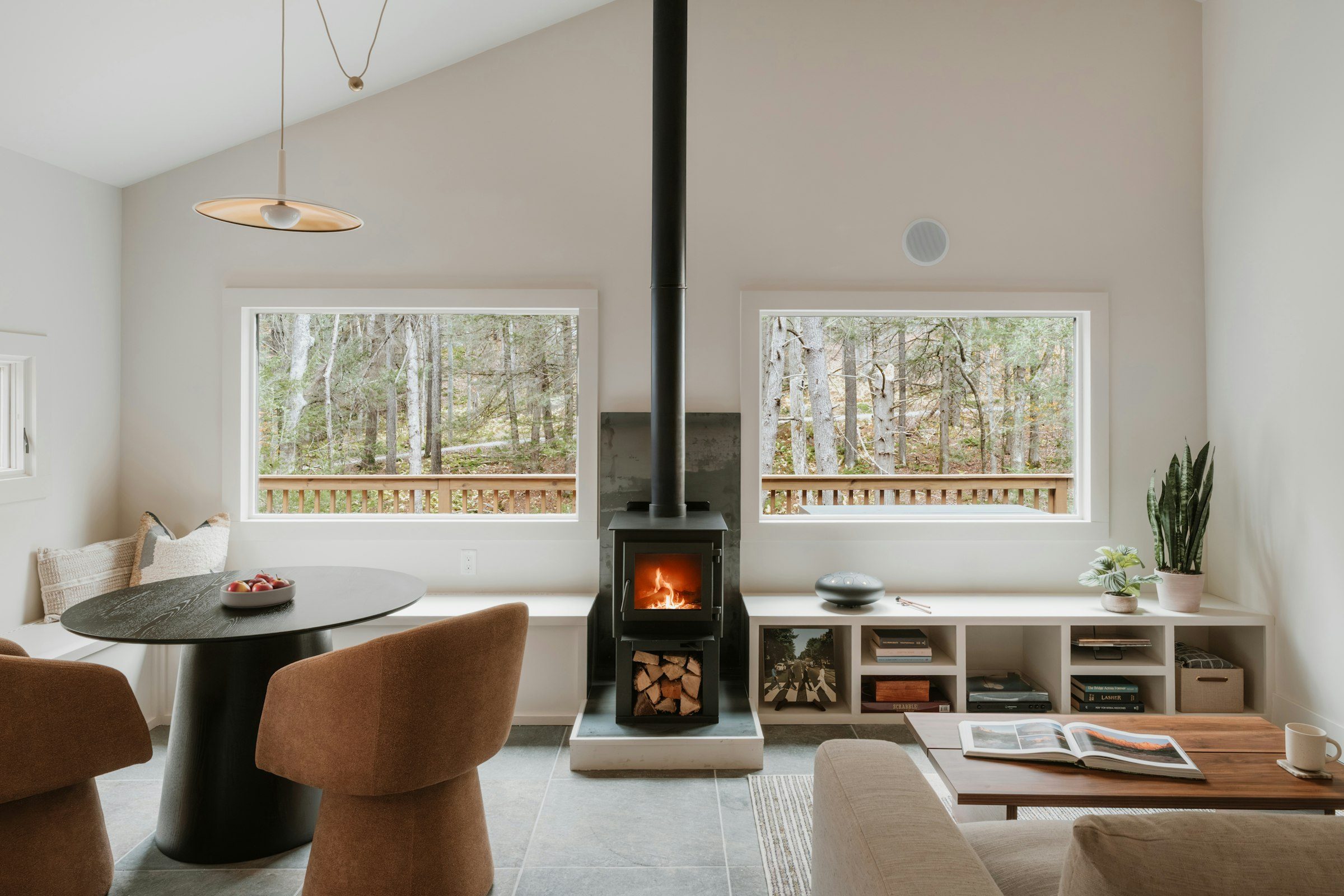 Rolig stue med vedovn og store vinduer mot skogen